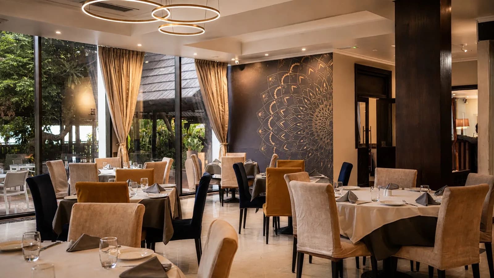 The Alcove dining room — warm lighting, ring chandeliers, a golden mandala wall and a garden view